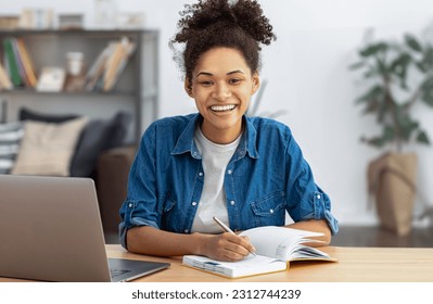 Happy female student using laptop computer, studying, distance learning or online education, looking at the camera smiling friendly. African American woman freelancer working from home - Shutterstock ID 2312744239
