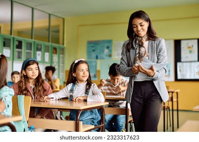 Happy female teacher giving test results to elementary students on a class in the classroom. - Powered by Shutterstock