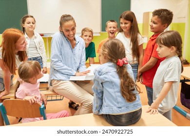 Happy female teacher holding book while sitting on bench with students in classroom - Powered by Shutterstock