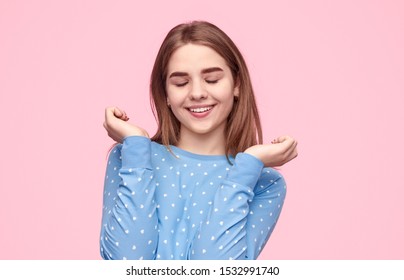 Happy Female Teenager In Blue Pajama Smiling And Closing Eyes While Being Awake Early In Morning Against Pink Background