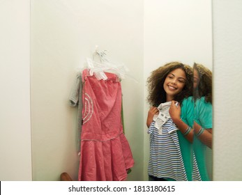 A Happy Female Teenager In Front Of A Mirror Trying Out New Clothes In The Trial Room.