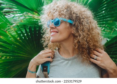 Happy female tourist with backpack enjoy nature park and smile agains a green big tropical leaf background. People and spring vacation. outdoor leisure activity. Portrait of happy woman outdoors - Powered by Shutterstock