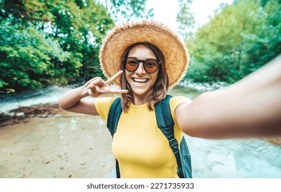 Happy female tourist with backpack taking selfie picture with smart mobile phone outside - Millenial woman having fun on adventure trip - Traveling and technology concept - Powered by Shutterstock