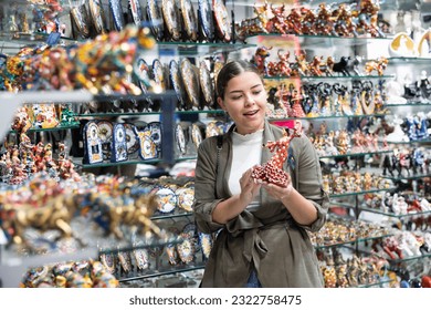Happy female tourist chooses Spanish handmade souvenirs - figurines of flamenco dancers displayed in a shop for sale