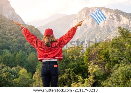 A happy female tourist with a Greek flag in her hands walks along the path to the top of the famous mythological Mount Olympus. Natural parks and attractions of Greece