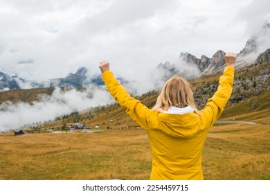 Happy female tourist spreads hands and enjoys in Italian Alps. Young woman feels happy to see Passo Giau pass in haze