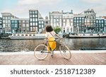 Happy female tourist visiting Amsterdam city, Netherlands - Delightful woman riding bicycle in urban street - Holidays, traveling and transportation life style concept