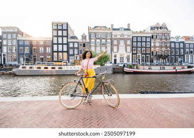 Happy female tourist visiting Amsterdam city, Netherlands - Delightful woman riding bicycle in urban street - Holidays, traveling and transportation life style concept