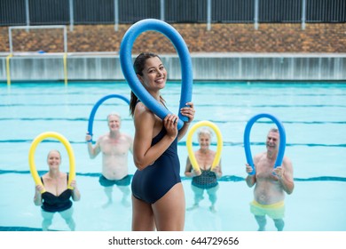 Happy female trainer and senior swimmers holding pool noodles - Powered by Shutterstock