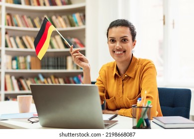 Happy Female Tutor Sitting At Table With Flag Of Germany, Using Laptop Computer, Teaching Foreign Language Online. Modern Remote Education, Abroad Work And Citizenship Concept