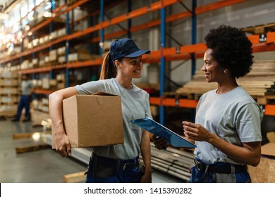 Happy Female Warehouse Workers Talking To Each Other While Preparing Shipment For Distribution In Industrial Warehouse. 