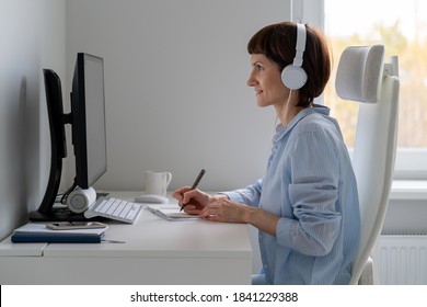 Happy Female In Wireless Headphones Studying Online Course, Using Pc And Writing In Notepad, Copy Space. Gig Economy, Digital Nomad, Distance Education. Side View Of Mature Woman Work From Home