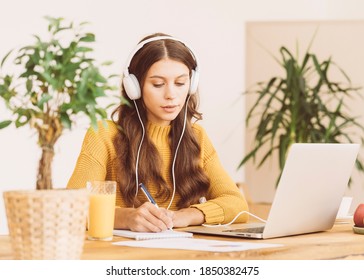 Happy Female In Wireless Headphones Studying Online Course And Writing In Notepad, Copy Space. Gig Economy, Digital Nomad, Distance Education. 