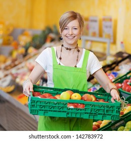 Happy Female Worker In A Supermarket Holding A Large Plastic Tray Of Fresh Produce In Her Hands