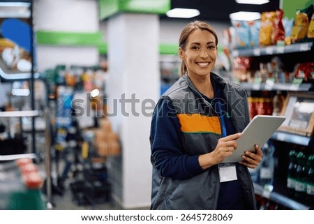 Happy female worker using digital tablet in a supermarket and looking at camera. Copy space. 