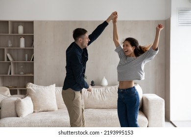 Happy Festive Millennial Generation Hispanic Latin Family Couple Dancing To Disco Music In Living Room, Celebrating Freedom. Bonding Loving Young Man And Woman Having Fun, Enjoying Domestic Activity