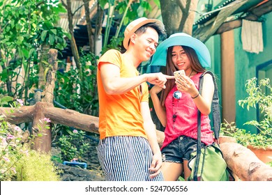 Happy filipino couple of tourists using mobile with man pointing at device screen - Young asian teenagers holding smart phone standing outdoors at summer day - Tourism and modern technology concept