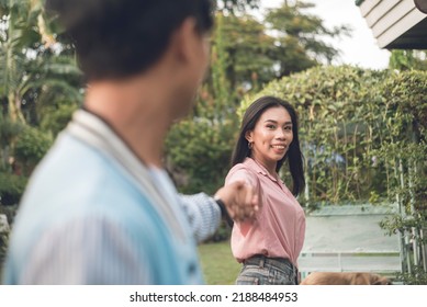 A Happy Filipino Woman Playfully Leads Her Boyfriend By The Hand, Leading The Way. Outdoor Scene.