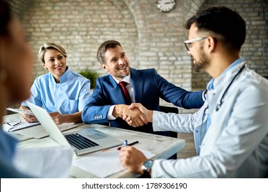 Happy financial advisor and male doctor shaking hands after successful meeting in the office.