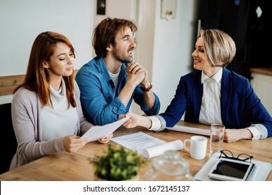 Happy Financial Advisor And Young Couple Analyzing Documents And Talking During A Meeting At Home. 