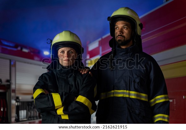 Happy firefighters man and woman\
after action looking at camera with fire truck in\
background
