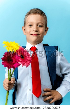 a happy first grader in a white shirt with a backpack holds a bouquet of flowers in his hands. Cute Caucasian boy goes to school with a bouquet of flowers and a backpack. Schoolboy. September 1