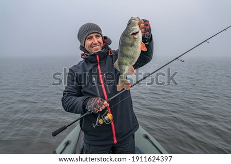 Happy fisherman hold big perch fish at boat with tackle. Success fishing at wild lake