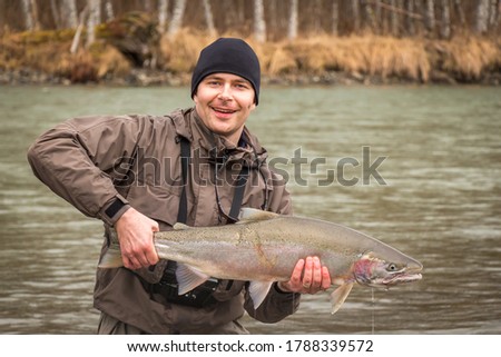 A happy fisherman holding up a fresh steelhead, rainbow trout, with a predator scar on its side, from the Kalum River, near Terrace, British Columbia, Canada