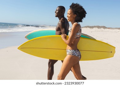 Happy, fit african american couple carrying surfboards walking on sunny beach to the sea. Summer, healthy lifestyle, sport, hobbies, surfing and vacation, unaltered. - Powered by Shutterstock