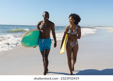 Happy, fit african american couple carrying surfboards walking on sunny beach by the sea. Summer, healthy lifestyle, sport, hobbies, surfing and vacation, unaltered. - Powered by Shutterstock