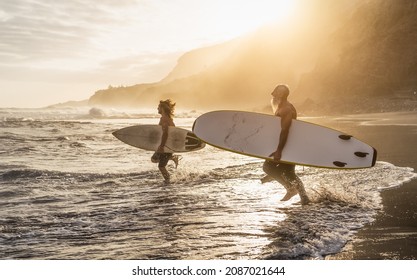 Happy fit friends surfing together on tropical beach at sunset time - People lifestyle and extreme sport concept - Powered by Shutterstock