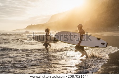 Happy fit friends surfing together on tropical beach at sunset time - People lifestyle and extreme sport concept