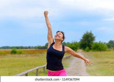 Happy Fit Middle Aged Woman Cheering And Celebrating As She Walks Along A Rural Lane  After Working Out Jogging In A Close Up View