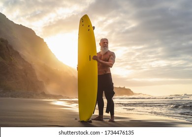 Happy fit senior having fun surfing at sunset time - Sporty bearded man training with surfboard on the beach - Active elderly people lifestyle and extreme sport concept - Powered by Shutterstock