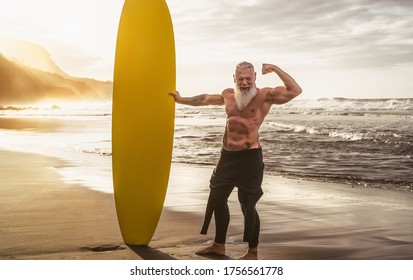 Happy Fit Senior Having Fun Surfing At Sunset Time - Sporty Bearded Man Training With Surfboard On The Beach - Elderly Healthy People Lifestyle And Extreme Sport Concept