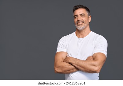 Happy fit sporty older man coach, middle aged sportsman athlete or personal trainer wearing white t-shirt showing muscles standing isolated on gray background advertising gym membership. Portrait.