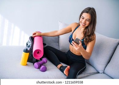 Happy Fit Woman Counts Calories And Made Post In Blog After Fitness Workout. Healthy Girl Wearing Sportwear Hold Smartphone In Hand And Considers Calories In Sport App Aftrer Training.