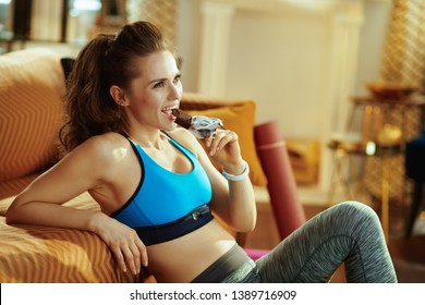 Happy Fit Woman In Sport Clothes In The Modern House Eating Chocolate Raw Protein Bar.