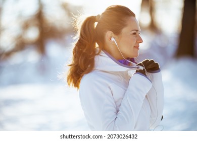 Happy Fit Woman In White Jacket With Headphones Outside In The City Park In Winter.