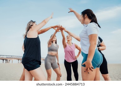 Happy fitness class giving high five after completing workout on beach. Multi aged women motivated after session together, engaged in team building, join hands for shared goal or success at training. - Powered by Shutterstock