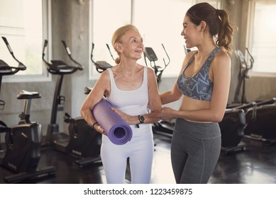 Happy Fitness Couple Senior And Young Woman Holding Yoga Mats And Walking In Class Of Fitness Gym.