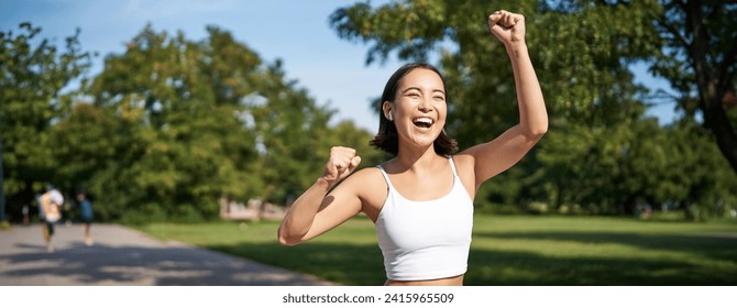 Happy fitness girl achieve goal, finish marathon, running with hands up, celebrating victory while jogging, triumphing in park. - Powered by Shutterstock