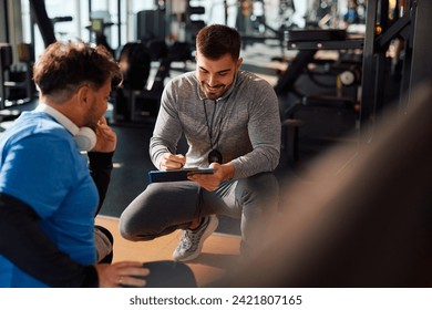 Happy fitness instructor preparing training plan for mature man's exercise class in a gym.  - Powered by Shutterstock