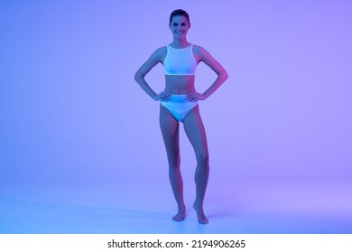 Happy Fitness Woman Posing In Blue Neon Light With Hands On Waist On Copy Space Background Showing Athletic Body And Training Results, Flat Stomach And Toned Legs