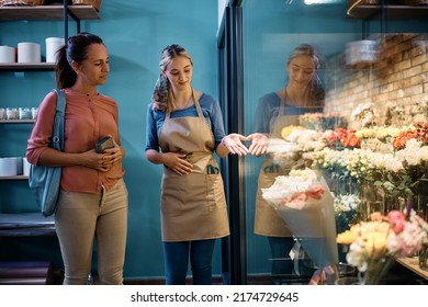 Happy Florist Showing Her Customer Flowers At Flower Cooler At The Shop.