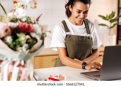 Happy Flower Shop Owner Working At The Counter. Female Florist Checking Online Orders On A Laptop.