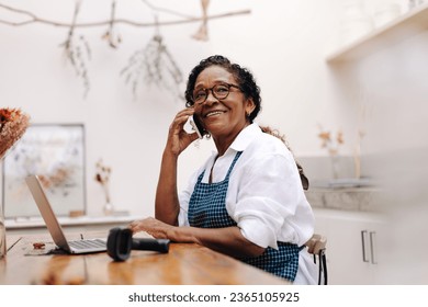 Happy flower store owner talks with her clients on a phone call, using her communication skills to build strong relationships with her customers. Senior craftswoman running a small business. - Powered by Shutterstock