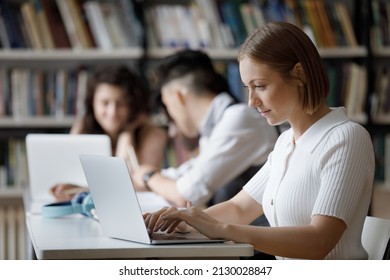 Happy focused smart Caucasian female student using computer writing essay or coursework, working on high school project, preparing for exams, sitting at shared table in public or college library. - Powered by Shutterstock