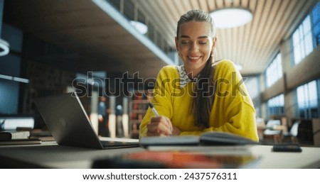 Happy and Focused Student Studying in a Modern Library. Young Female Enjoying Time Alone for Thinking and Problem Solving. Girl Using Laptop Computer to Work on a University Research Project Online
