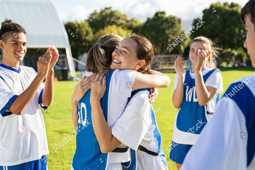 Happy football players hugging on field after scoring a goal. Soccer teammates embracing while players clapping hands on victory. Successful girl soccer players celebrating after winning the match.